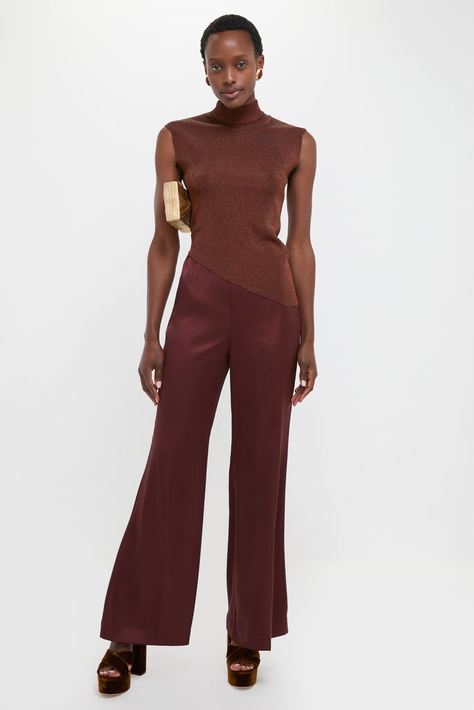 Model in a Rust Edith Top, a classic sleeveless high-neck design with an asymmetrical hem, paired with wide-leg satin trousers. Effortless and high-end style.