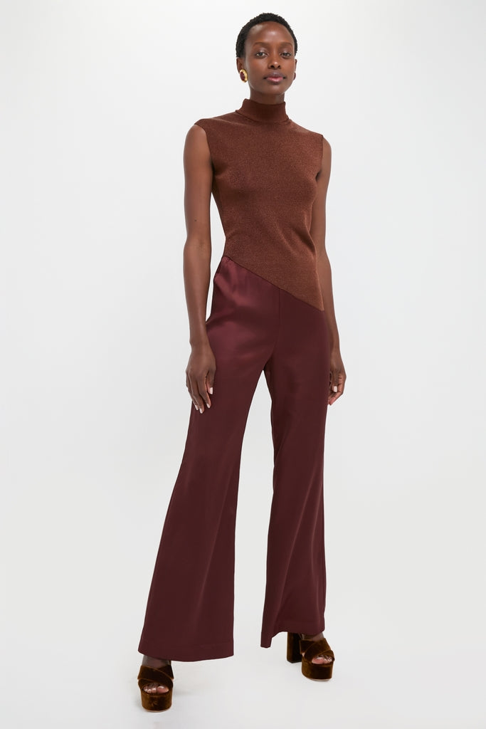 Woman models classic Rust Edith Top with angular hemline, paired with high-waisted burgundy trousers and chunky platform heels, embodying effortless, high-end fashion and fun style.