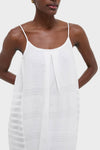 Woman in a classic, effortless Abira White Nia Slip Dress with spaghetti straps, textured stripes, and gold hoop earring, exuding a fun, high-end vibe.