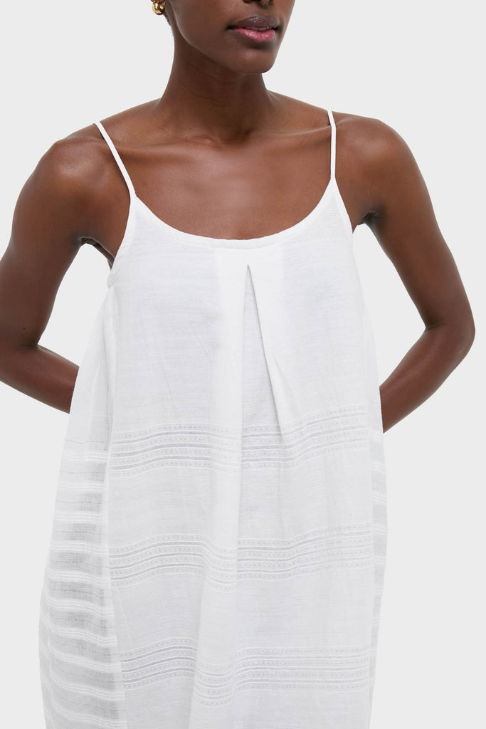 Woman in a classic, effortless Abira White Nia Slip Dress with spaghetti straps, textured stripes, and gold hoop earring, exuding a fun, high-end vibe.