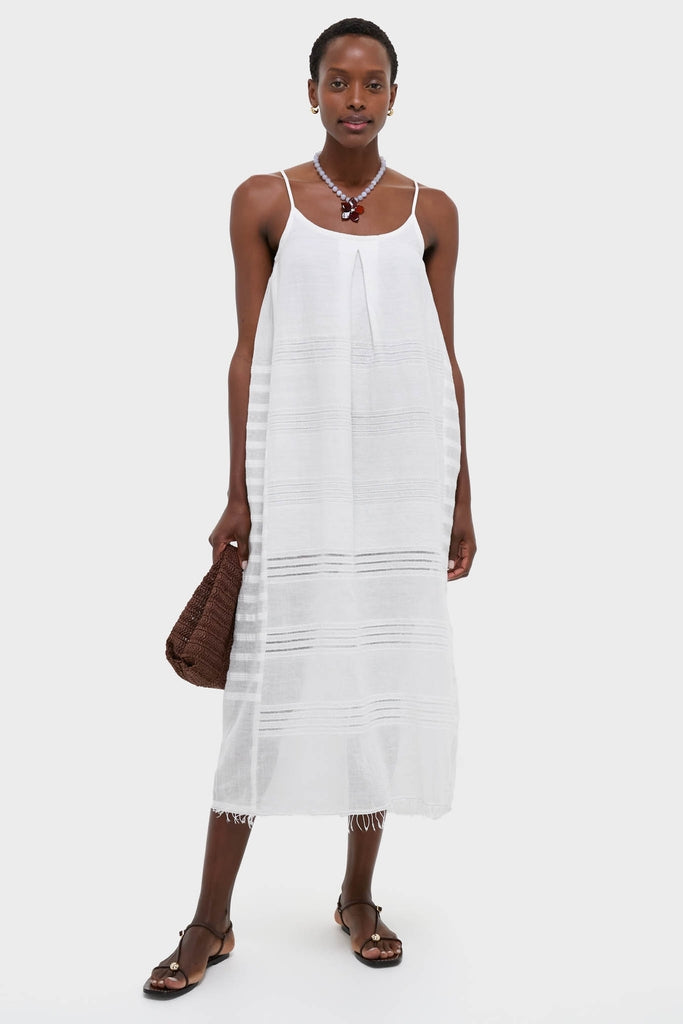 Woman in a classic, effortless Abira White Nia Slip Dress with textured stripes, accessorized with a chunky necklace, holding a woven tote, embodying high-end, fun style.