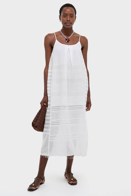 Woman in a classic, effortless Abira White Nia Slip Dress with textured stripes, accessorized with a chunky necklace, holding a woven tote, embodying high-end, fun style.