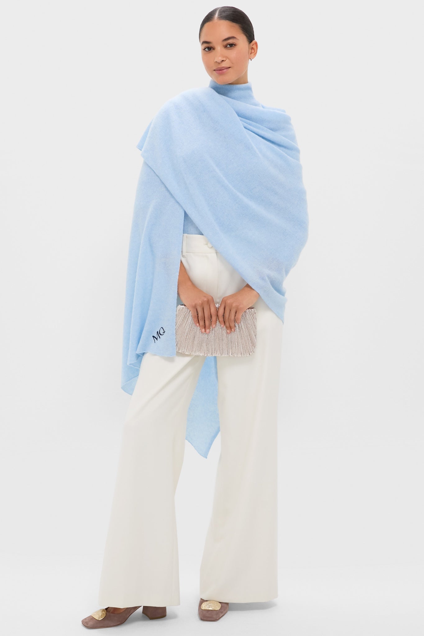 Woman elegantly models an Ice Blue Cashmere Blanket Scarf, exuding classic, high-end style. It's draped over ivory trousers, paired with a fun fringed clutch and effortless loafers.