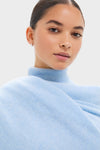 Young person in light-blue turtleneck showcases an Ice Blue Cashmere Blanket Scarf, epitomizing effortless, high-end style with its classic, luxurious cashmere softness.