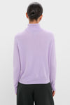 Woman in a classic Lavender Frost Cashmere Turtleneck Sweater, showcasing its effortless elegance, paired with loose-fit black trousers for a high-end, fun look.