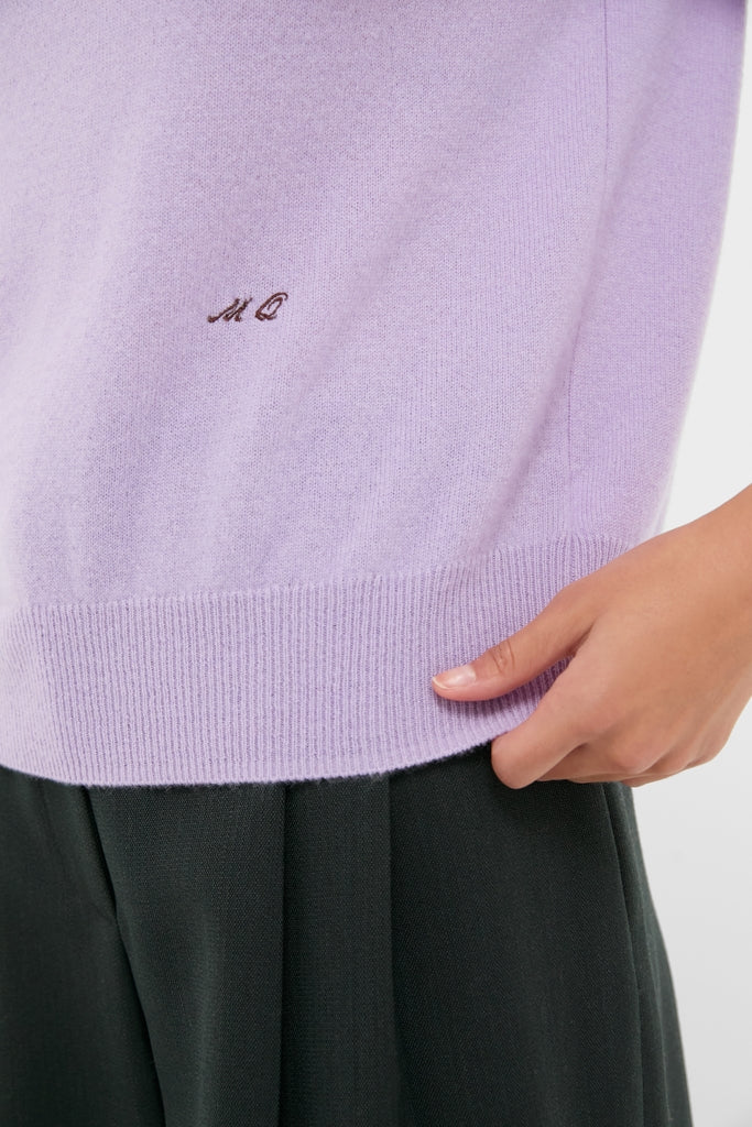 Lavender Frost Cashmere Turtleneck Sweater, featuring a classic embroidered “MO” logo above the hem, paired effortlessly with a dark pleated skirt for a high-end, fun look.