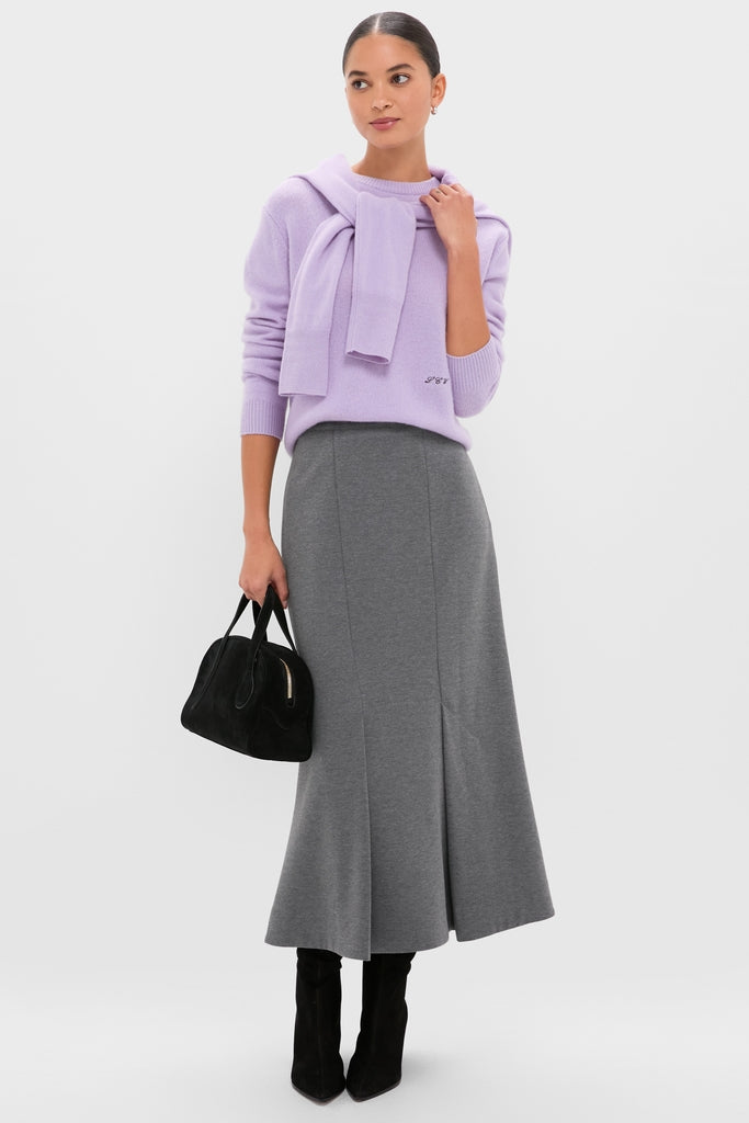 Woman wearing a classic Lavender Frost Cashmere Boyfriend Bodie Crewneck Sweater, paired effortlessly with a gray midi skirt, black suede ankle-boots, and a high-end black handbag.