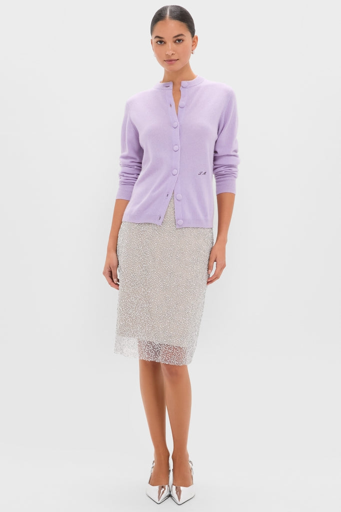 Woman wearing the Lavender Frost Cashmere Quinn Cardigan, a classic, soft lavender button-up with round neckline, paired with a semi-sheer dotted skirt and metallic heels. Effortless, high-end style.