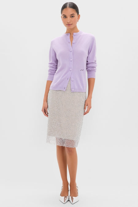 Woman wearing the Lavender Frost Cashmere Quinn Cardigan, a classic, soft lavender button-up with round neckline, paired with a semi-sheer dotted skirt and metallic heels. Effortless, high-end style.