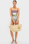 Woman in a colorful swimsuit holds a high-end woven straw beach tote, accessorized with a classic Fish Raffia Bag Charm, embodying effortless, fun style.