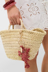 Close-up of a classic Lobster Raffia Bag Charm in terracotta, effortlessly hanging from a woven straw tote, embodying fun and high-end style with a playful lobster design.