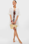 Model in white eyelet-lace cover-up and brown swimsuit, holding a woven straw tote with a classic, fun Lobster Raffia Bag Charm, embodying effortless, high-end style.