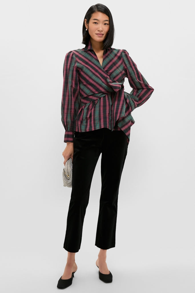 Woman models the classic Tartan Tie Front Bow Bea Blouse, featuring an effortless wrap style and peplum waist, paired with sleek black velvet pants and a chic clutch.