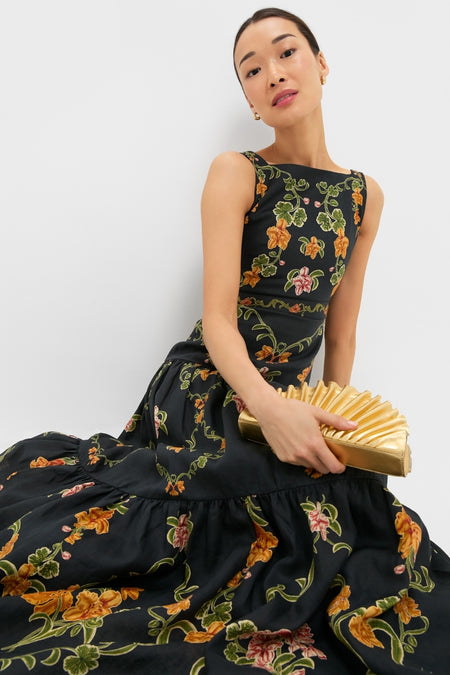 Cordillera Abeja Maxi Dress: Classic black dress with green vines and vibrant blooms, paired with a gold clutch. Effortless, high-end style for fun, confident elegance.