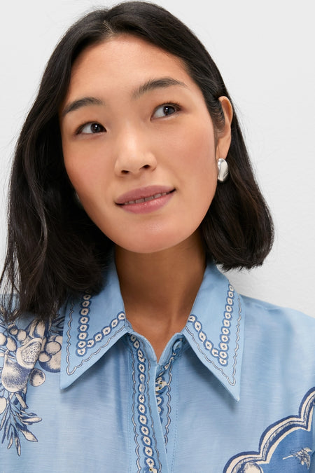 Young woman in a light-blue Blue Villa Romantica Mini Dress with embroidered details, wearing a chunky silver heart-shaped earring, embodying Tuckernuck's classic and effortless style.