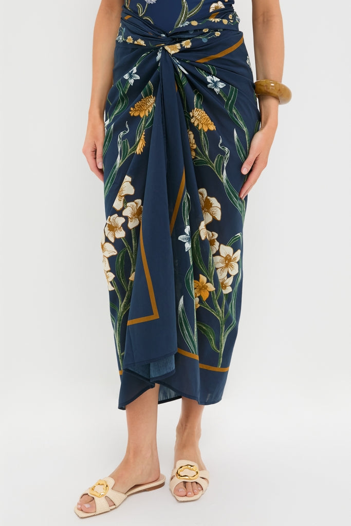 Laguna Lavanda Midi Sarong: A classic navy wrap skirt with floral print, knotted at the waist, paired with light slide sandals and an amber bangle for an effortless, high-end look.