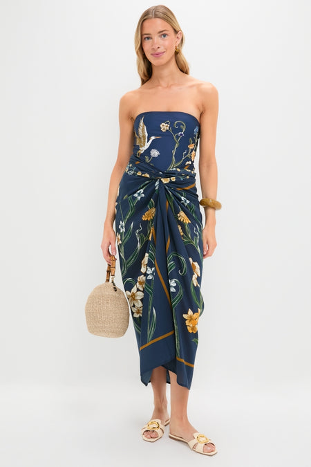 Laguna Lavanda Midi Sarong: Effortless, classic navy-blue dress with botanical-bird motif, gathered waist, and high-end style, paired with fun straw handbag and simple gold accessories.
