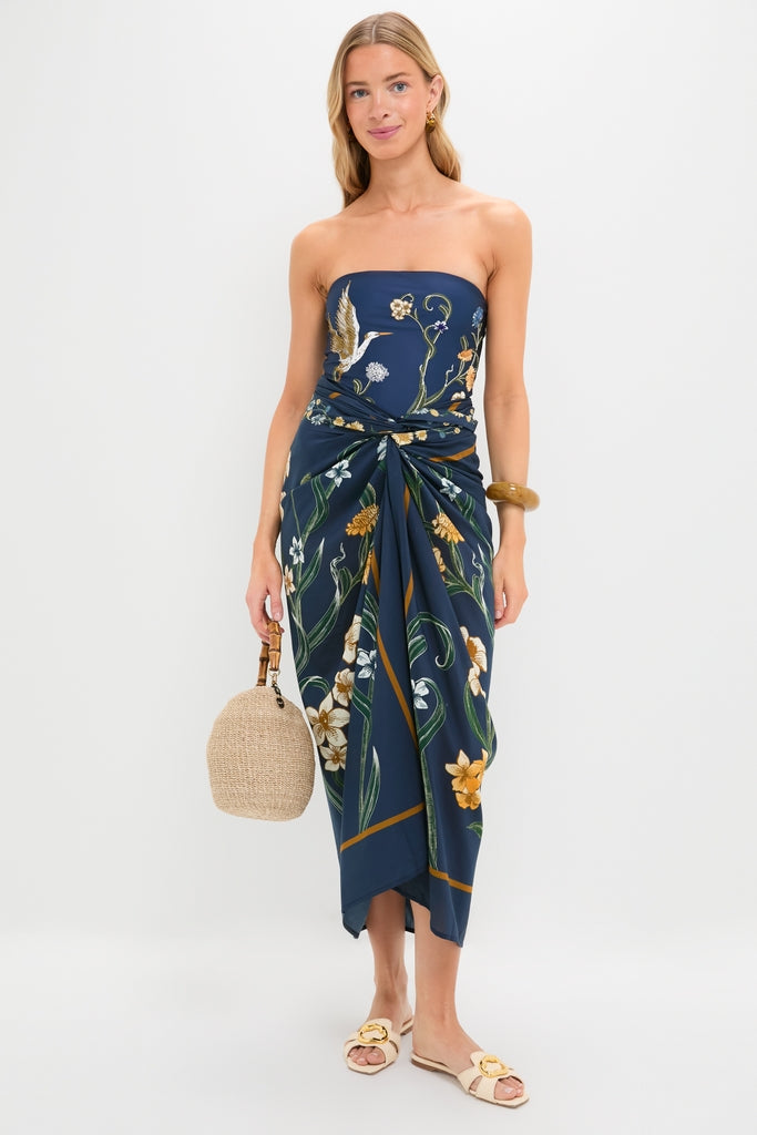 Laguna Lavanda Midi Sarong: Effortless, classic navy-blue dress with botanical-bird motif, gathered waist, and high-end style, paired with fun straw handbag and simple gold accessories.