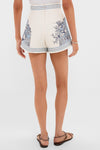 Woman in high-waisted Cream Villa Romantica Corset Shorts with blue toile print, showcasing effortless elegance and classic style. Paired with white top and dark brown sandals.
