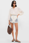 Woman in classic Cream Villa Romantica Corset Shorts with blue toile print and raffia buttons, styled effortlessly with an ivory blouse, exuding high-end, fun, resort-ready elegance.