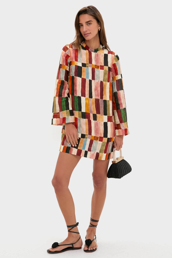 Woman wearing the classic Multi Marjorelle Mini Dress with a relaxed silhouette and beaded detail, styled effortlessly with black sandals and a high-end wicker clutch.