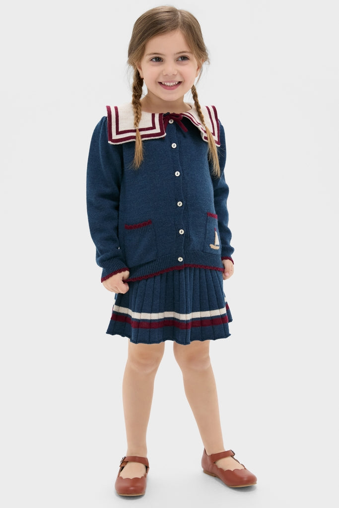 Young girl in a classic, high-end Mariner Collar Cardigan in Navy, featuring effortless nautical details like a boat motif and burgundy accents, embodying fun and timeless style.