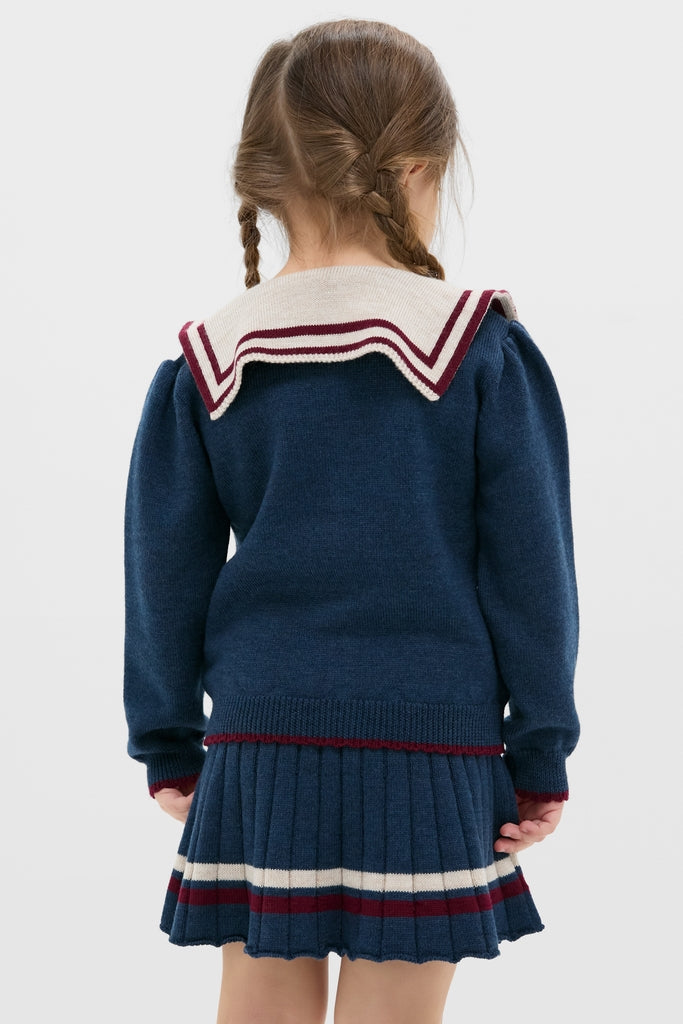 Young girl in classic, high-end Mariner Collar Cardigan in Navy, showcasing effortless nautical style with playful boat embroidery and fun burgundy bow detail.