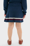 Child wearing the Pleated Knit Skirt in Navy with elegant pleats and a burgundy bow detail, embodying a classic, effortless style perfect for fun, high-end autumn looks.