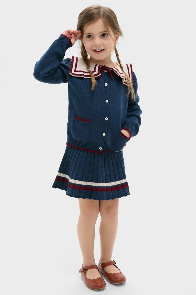 Young girl in a navy Pleated Knit Skirt with burgundy bow, embodying a classic, effortless style, paired with a fun Mariner Collar Cardigan.