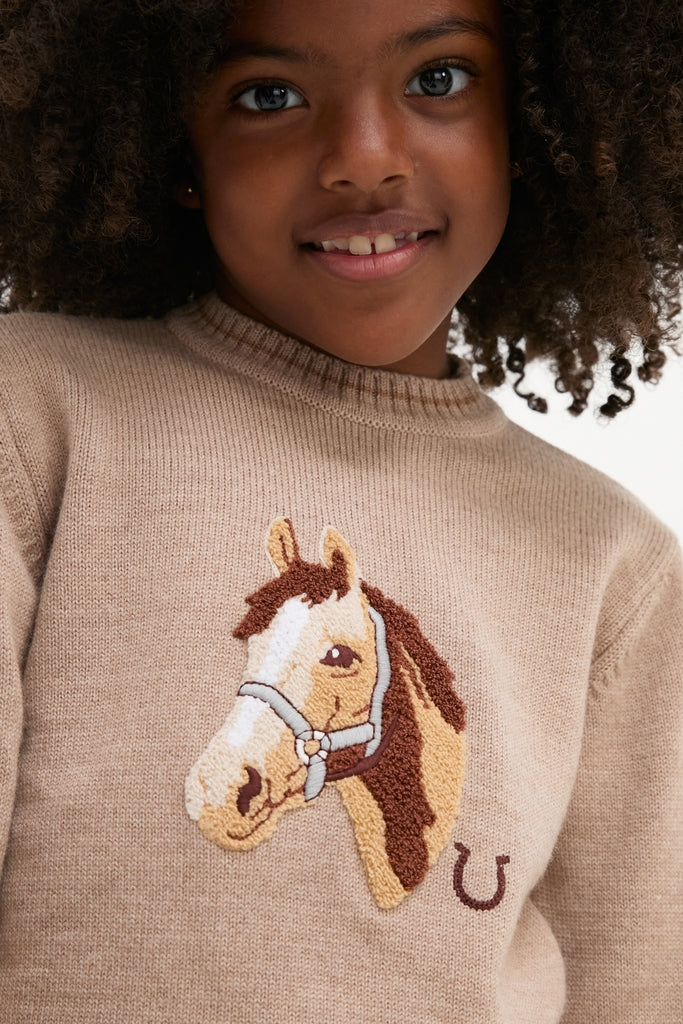 Young girl wearing the Jacquard Head Horse Jumper, a classic, high-end beige knit sweater with an embroidered horse motif, offering effortless style and fun for everyday wear.