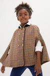 Young girl in a classic, high-end brown-and-blue checked double-breasted cape with velvet collar and gold buttons, exuding effortless confidence and timeless elegance.