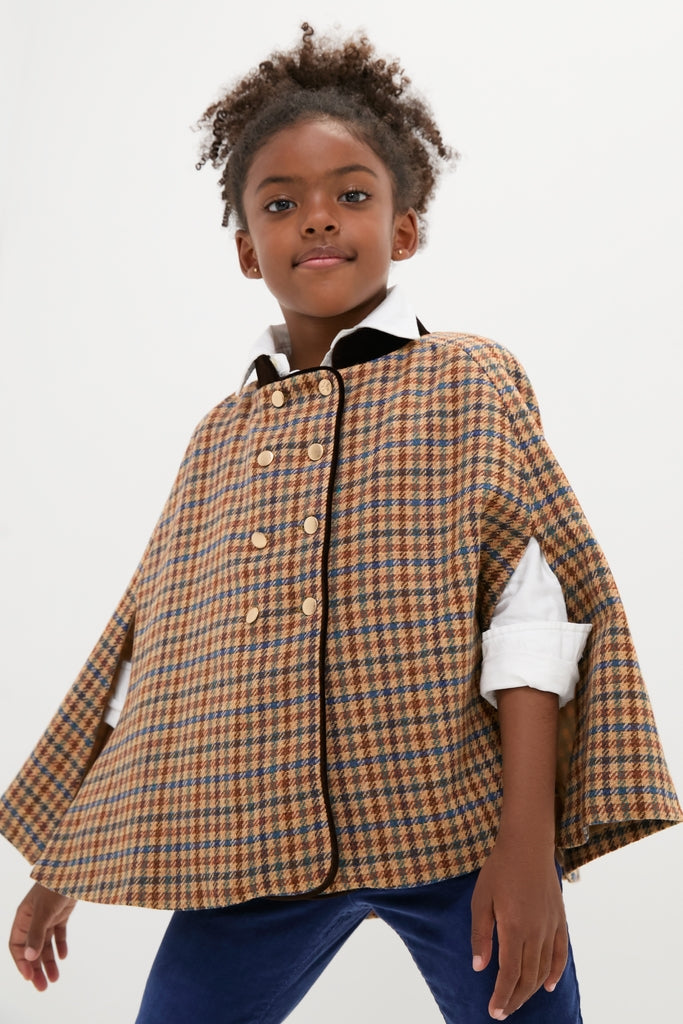 Young girl in a classic, high-end brown-and-blue checked double-breasted cape with velvet collar and gold buttons, exuding effortless confidence and timeless elegance.