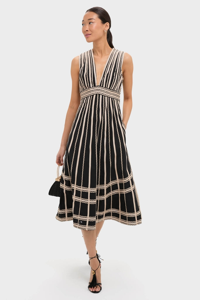Model in Noir Palermo Dress: classic A-line midi with deep V-neck, contrasting cream stripes, holding black handbag. Effortless elegance, perfect for a fun, high-end look.