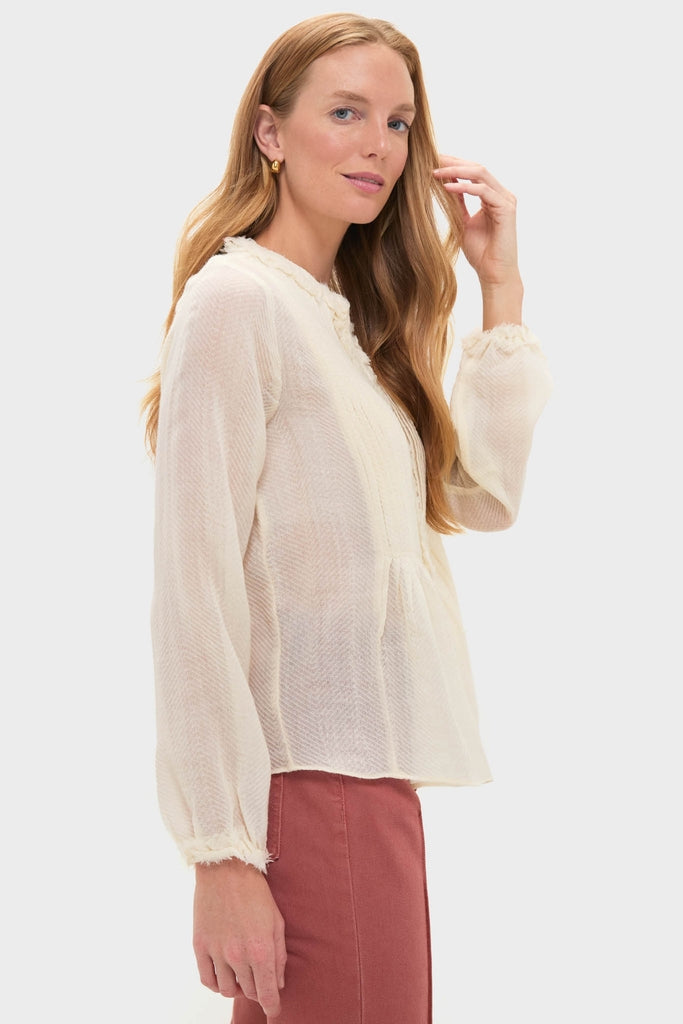 Model wearing Cowrie Adriel Blouse, a classic, semi-sheer ivory top with pintuck details and frayed cuffs, paired with high-waisted terracotta bottoms, exuding effortless, high-end style.
