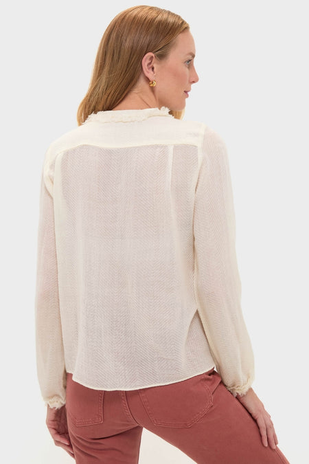 Woman wearing Cowrie Adriel Blouse, a classic, effortless cream blouse with herringbone texture, frayed-edge trim, and gathered cuffs, paired with high-waisted rust jeans.