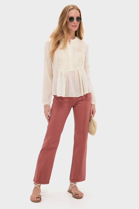 Model wearing the Cowrie Adriel Blouse, featuring pintuck details and a peplum hem, paired with high-waisted terra-cotta jeans, embodying a classic, effortless, and high-end look.
