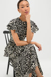 Spotted Jasper Amaia Dress on a seated woman, showcasing its classic fit-and-flare design, effortless flutter sleeves, and high-end tiered ruffles, perfect for fun, versatile occasions.