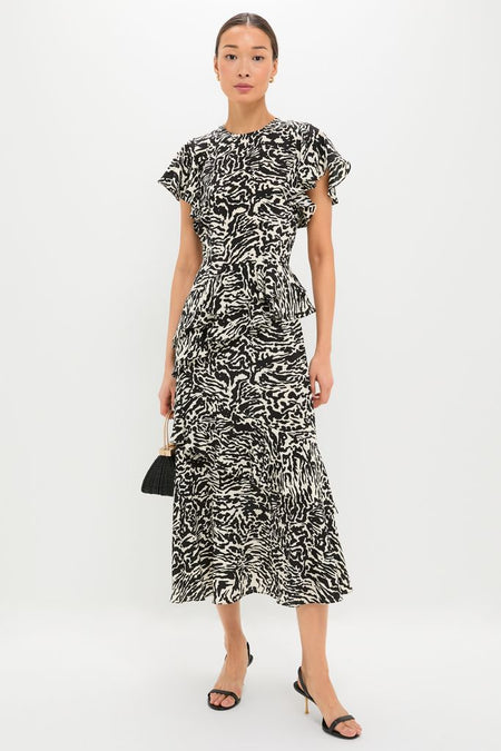 Model wearing the Spotted Jasper Amaia Dress, a classic, high-end silk midi with flutter sleeves and peplum, paired with a black handbag and strappy heels for an effortless, fun look.