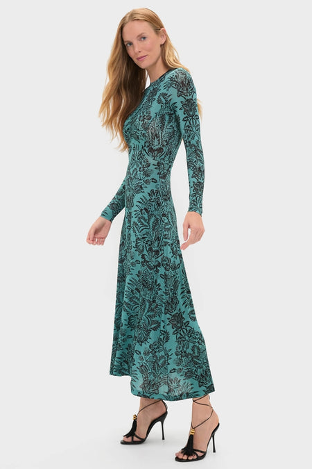 Model wearing the Ocean Flora Naia Dress, a classic, high-end teal-green dress with a black botanical print, styled with effortless black strappy sandals, embodying fun elegance.