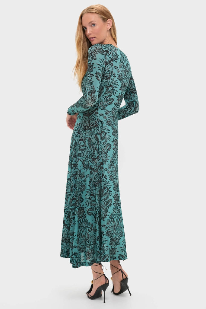 Model wearing the classic Ocean Flora Naia Dress, an effortless teal-green maxi with a black floral pattern, featuring a fitted bodice and gently flared skirt, styled with strappy heels.
