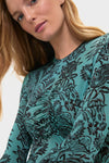 Model in Ocean Flora Naia Dress, a classic teal-green top with dark floral print and center ruching, embodying effortless, high-end style.