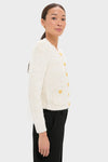 Woman in profile wears the classic Ivory Una Knit Cardigan with gold buttons and patch pockets, exuding effortless high-end style, paired with black trousers for a fun, polished look.