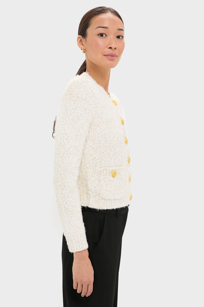 Woman in profile wears the classic Ivory Una Knit Cardigan with gold buttons and patch pockets, exuding effortless high-end style, paired with black trousers for a fun, polished look.