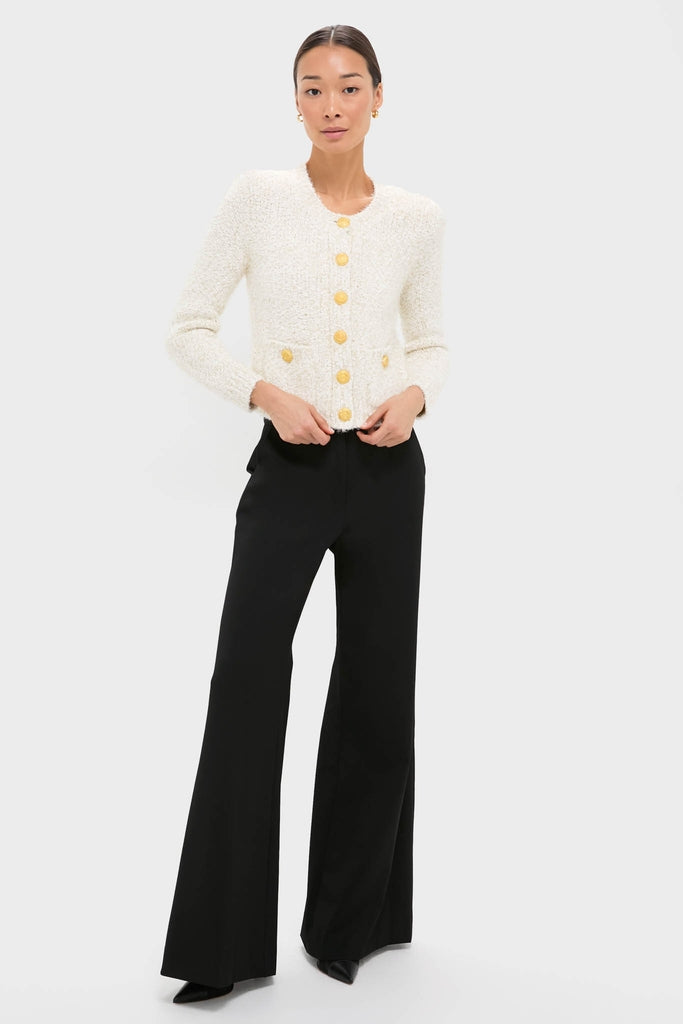 Woman in a classic Ivory Una Knit Cardigan with gold crest buttons, paired with high-waisted black trousers, exuding an effortless, high-end style.