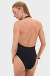Model in Noir Milos Maillot, a classic black one-piece with halter neckline, open back, and stone-embellished ring, showcasing effortless, high-end swimwear style.