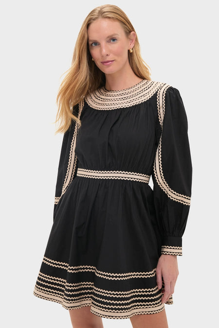 Model wearing the Noir Fiora Mini Dress, a classic, high-end black dress with playful zig-zag trim, effortlessly blending fun and sophistication with its voluminous silhouette.