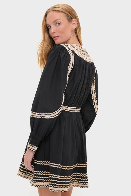 Young woman in a classic Noir Fiora Mini Dress with cream wavy trim, showcasing effortless style and fun elegance against a light backdrop.