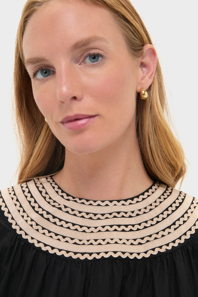 Woman wearing the Noir Fiora Mini Dress with classic cream ribbon trim, exuding an effortless, high-end style. Gold hoop earrings add a fun, subtle touch.