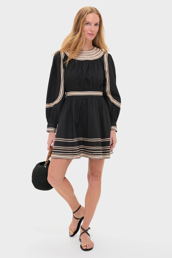 Model wearing the Noir Fiora Mini Dress with cream scalloped trim, effortlessly styled with a round black handbag and strappy sandals, embodies classic high-end fashion with a fun twist.