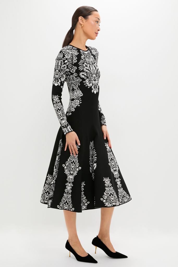Woman models the Noir Callista Dress, a classic black midi with a white floral motif, offering an effortless, high-end look, paired with fun, chic pointed-toe heels.